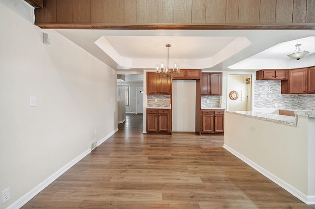 kitchen with light stone countertops, hardwood / wood-style floors, backsplash, hanging light fixtures, and a tray ceiling