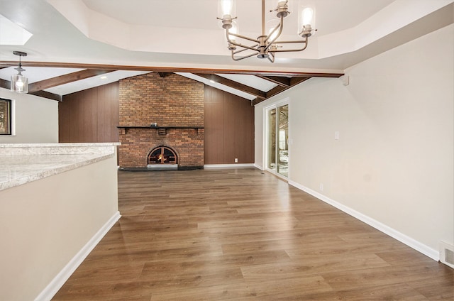 unfurnished living room featuring a brick fireplace, dark wood-type flooring, lofted ceiling with beams, and an inviting chandelier