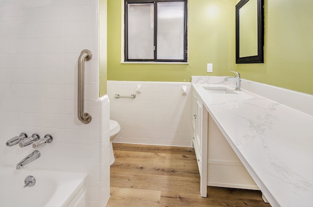 full bathroom with toilet, hardwood / wood-style flooring, shower / bathing tub combination, tile walls, and vanity