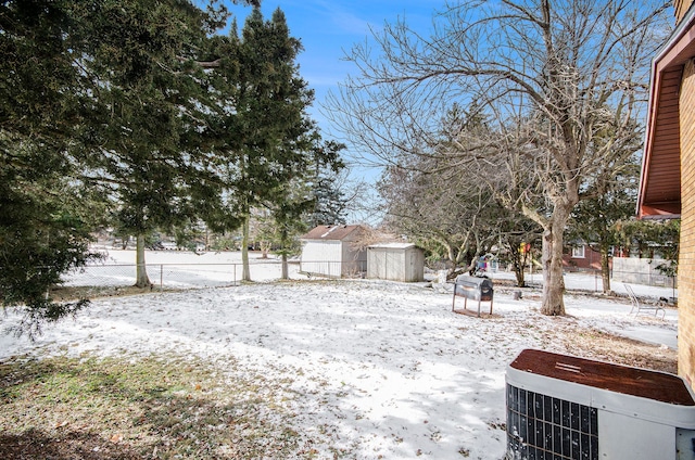 yard layered in snow featuring a storage shed and central AC