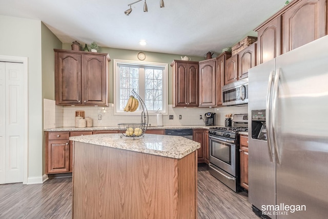 kitchen with a center island, decorative backsplash, light stone countertops, appliances with stainless steel finishes, and dark hardwood / wood-style flooring