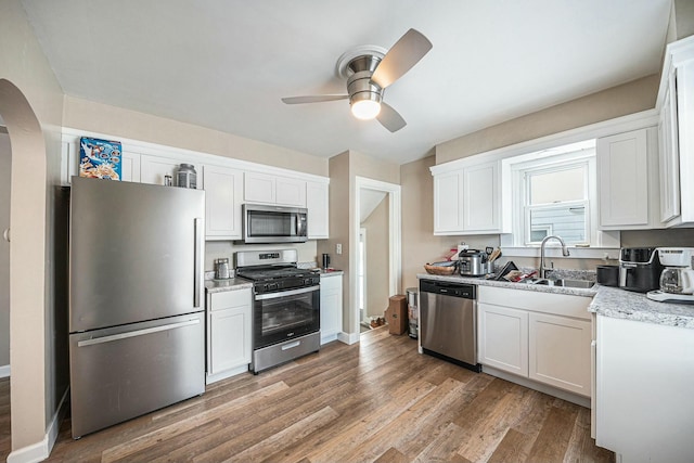 kitchen featuring light wood-style flooring, arched walkways, a sink, stainless steel appliances, and white cabinetry