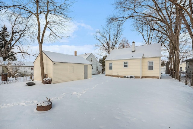 snow covered back of property with a chimney, a storage shed, an outdoor structure, and fence