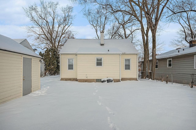 snow covered back of property featuring an outdoor structure and fence