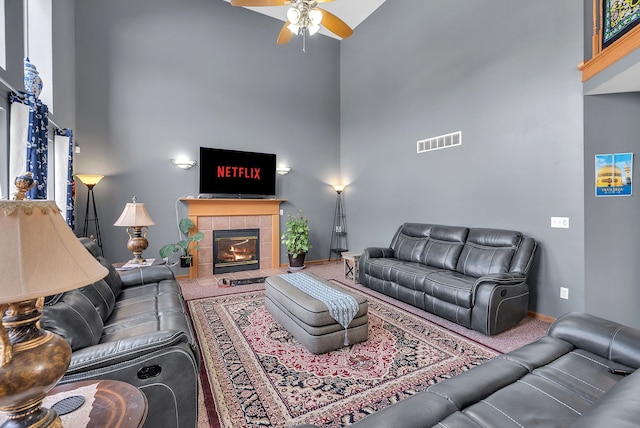 living room featuring ceiling fan, carpet, a tile fireplace, and a towering ceiling