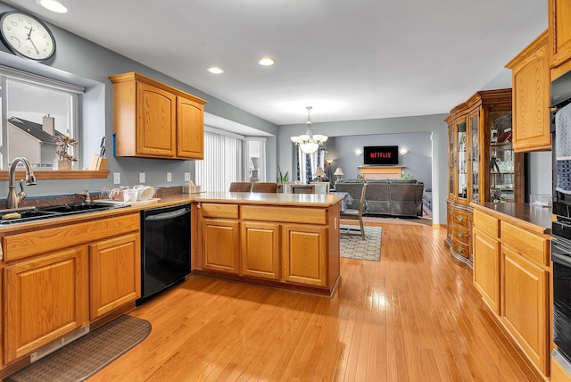 kitchen with pendant lighting, black appliances, kitchen peninsula, sink, and an inviting chandelier