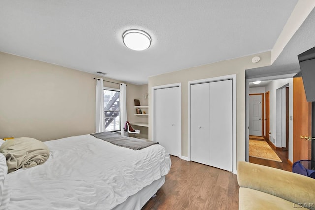 bedroom with multiple closets, a textured ceiling, and wood-type flooring