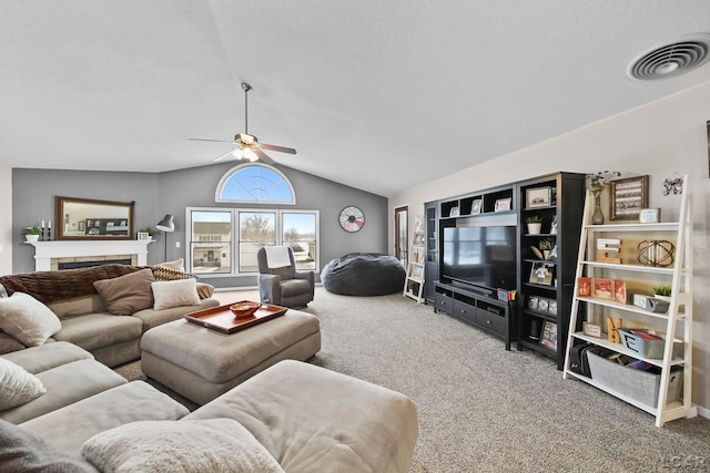 carpeted living room with ceiling fan, a tiled fireplace, a textured ceiling, and lofted ceiling