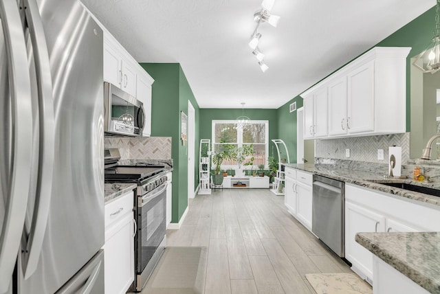 kitchen featuring stainless steel appliances, pendant lighting, white cabinets, and sink