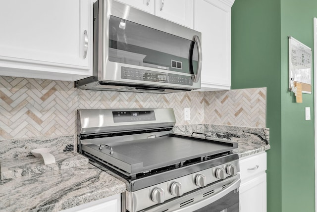 kitchen featuring stainless steel appliances, white cabinetry, tasteful backsplash, and light stone countertops