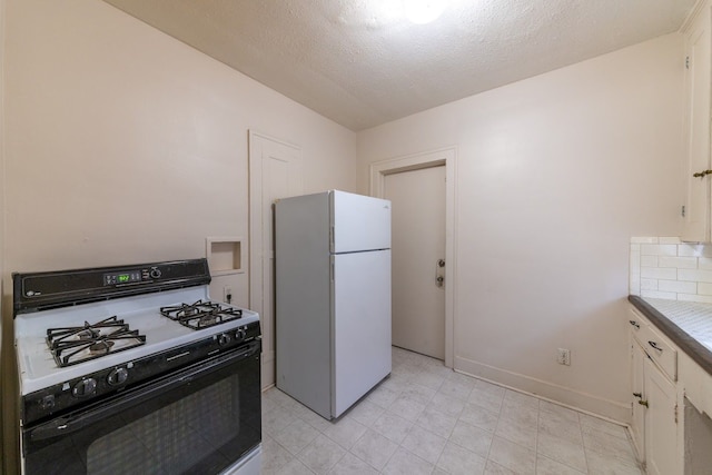 kitchen with white refrigerator, white cabinets, a textured ceiling, and gas range