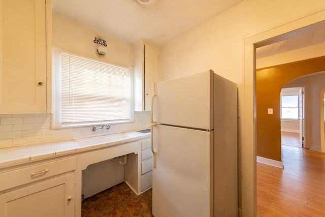 kitchen featuring sink, white refrigerator, backsplash, white cabinets, and tile countertops