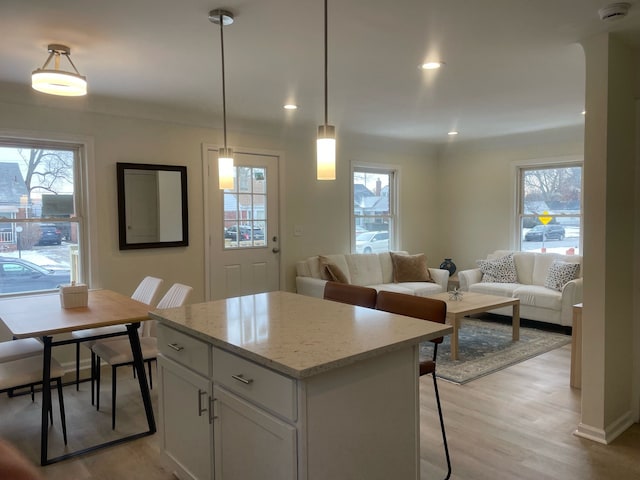 kitchen featuring white cabinets, decorative light fixtures, light wood-type flooring, a breakfast bar, and light stone counters