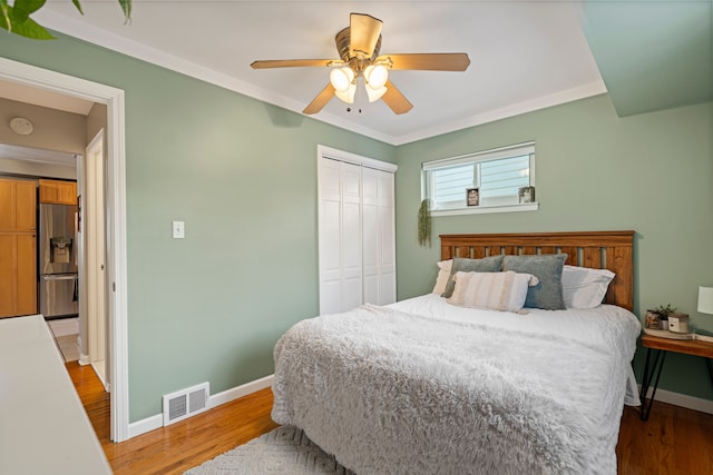 bedroom with light wood-type flooring, ornamental molding, stainless steel fridge, a closet, and ceiling fan