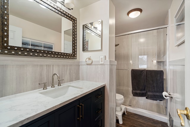 bathroom with a shower with shower door, wood-type flooring, tile walls, vanity, and toilet