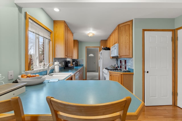 kitchen with tasteful backsplash, sink, white appliances, and light hardwood / wood-style floors