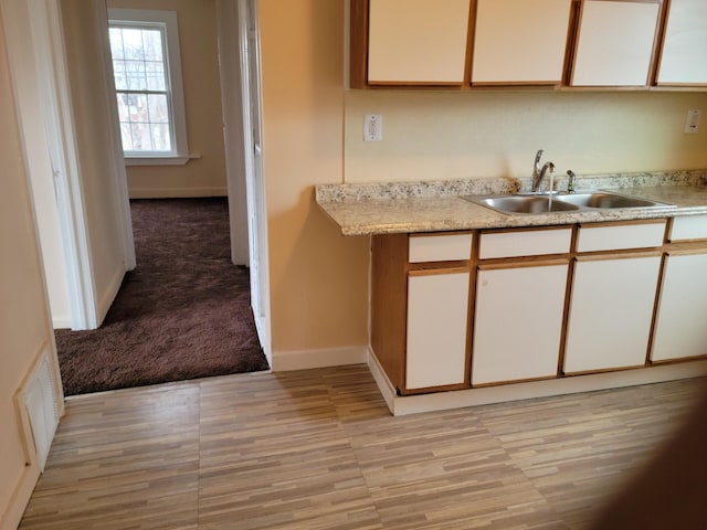 kitchen with light carpet, sink, and white cabinetry