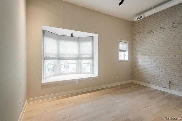 unfurnished room featuring ceiling fan, light wood-type flooring, and brick wall