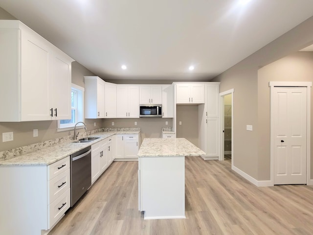 kitchen featuring white cabinetry, stainless steel appliances, a kitchen island, light stone counters, and sink