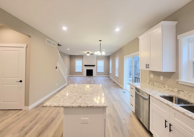 kitchen with a kitchen island, white cabinetry, hanging light fixtures, light stone counters, and stainless steel dishwasher