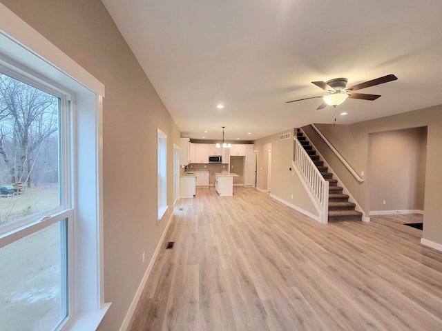 unfurnished living room with ceiling fan with notable chandelier and light hardwood / wood-style flooring