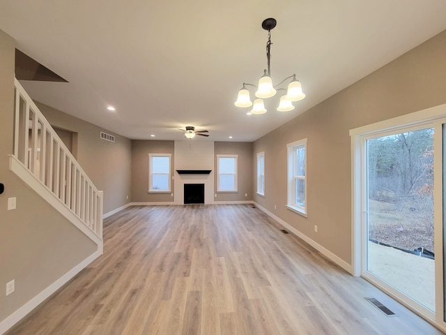 unfurnished living room featuring ceiling fan with notable chandelier, light hardwood / wood-style floors, and a wealth of natural light