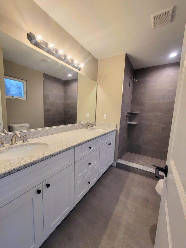 bathroom with toilet, tiled shower, and vanity