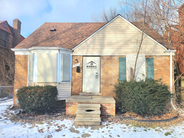 bungalow featuring brick siding and a shingled roof