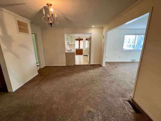 carpeted empty room featuring a textured ceiling, crown molding, and a notable chandelier