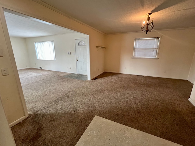 carpeted spare room featuring an inviting chandelier, a textured ceiling, and ornamental molding