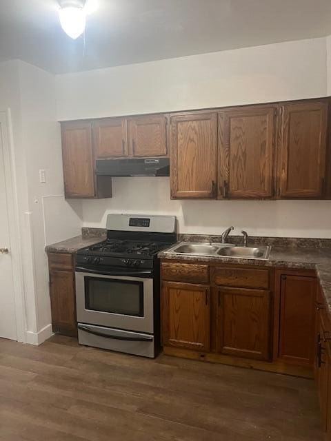 kitchen featuring gas stove, under cabinet range hood, a sink, dark countertops, and dark wood-style floors