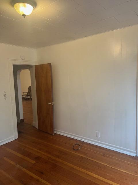 empty room with hardwood / wood-style flooring, arched walkways, and baseboards