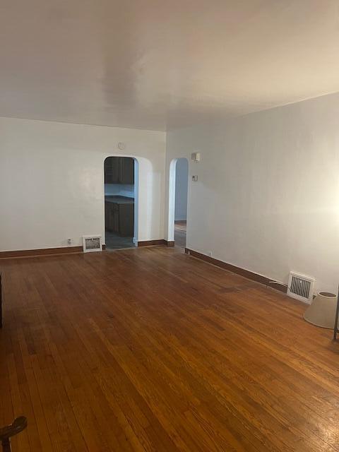 empty room featuring hardwood / wood-style floors, arched walkways, and baseboards