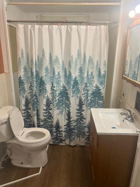 bathroom featuring toilet, wood finished floors, vanity, a shower with shower curtain, and tile walls