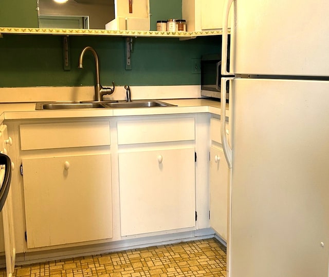 kitchen with freestanding refrigerator, a sink, light countertops, white cabinetry, and stainless steel microwave