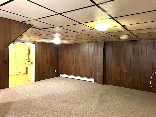 finished below grade area featuring carpet flooring, wood walls, a baseboard heating unit, and a drop ceiling