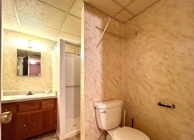 bathroom featuring vanity, a shower stall, toilet, and a paneled ceiling