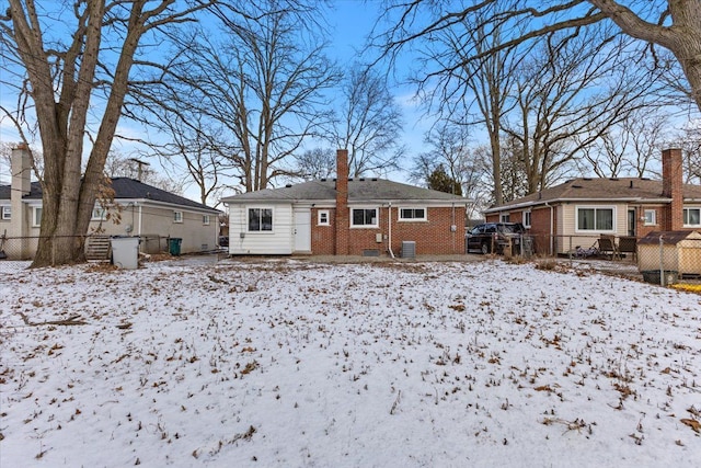 snow covered rear of property featuring an outbuilding, brick siding, fence, and a chimney