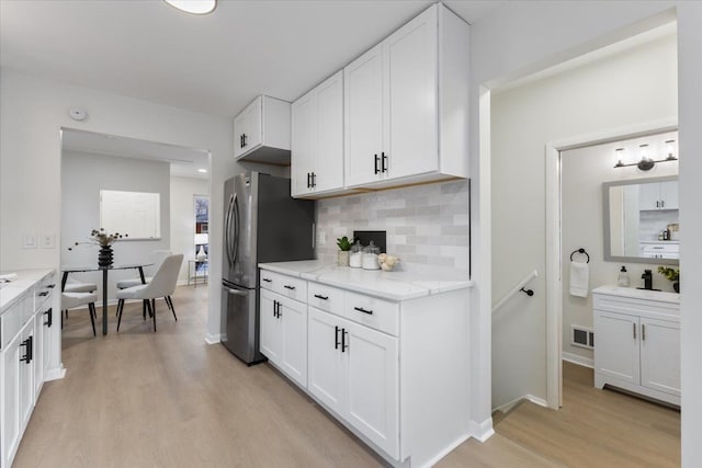 kitchen featuring light hardwood / wood-style floors, stainless steel fridge, backsplash, light stone countertops, and white cabinets