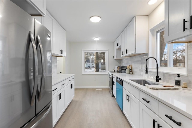 kitchen featuring white cabinets, stainless steel appliances, sink, backsplash, and light stone counters