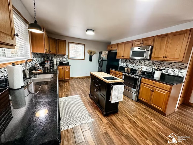 kitchen with appliances with stainless steel finishes, decorative light fixtures, sink, wood-type flooring, and a center island