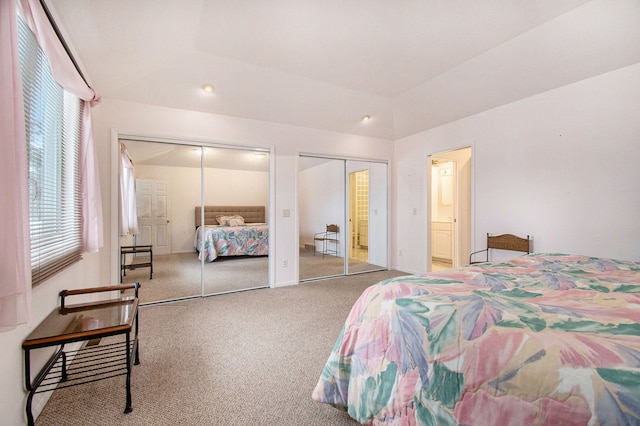 carpeted bedroom featuring two closets, vaulted ceiling, and ensuite bathroom