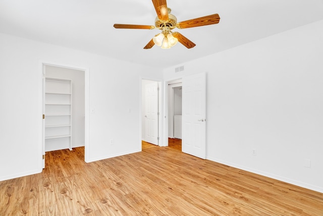 unfurnished bedroom featuring a walk in closet, light hardwood / wood-style floors, a closet, and ceiling fan