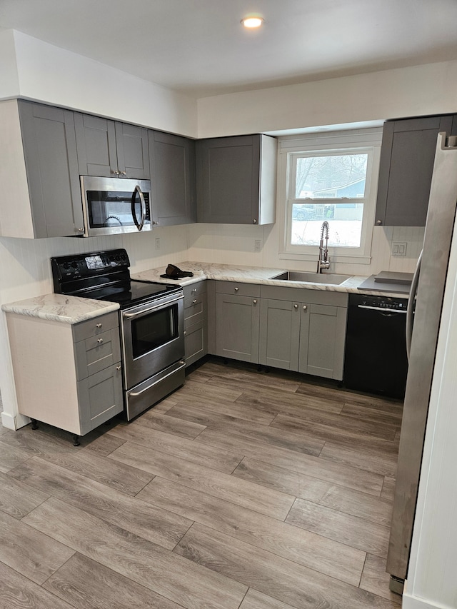 kitchen featuring light stone countertops, appliances with stainless steel finishes, light hardwood / wood-style flooring, sink, and gray cabinetry