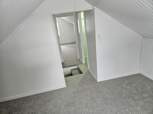 additional living space featuring lofted ceiling, wood walls, and dark colored carpet