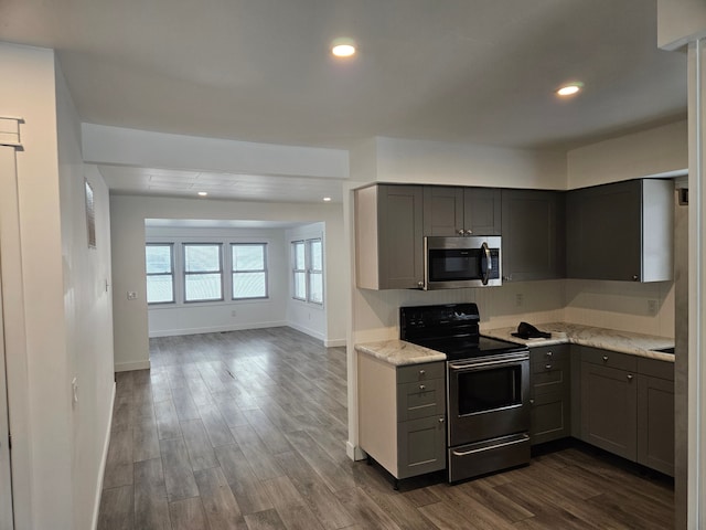 kitchen with appliances with stainless steel finishes, gray cabinetry, dark hardwood / wood-style flooring, and light stone counters