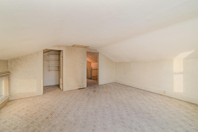 additional living space featuring carpet, vaulted ceiling, and a textured ceiling