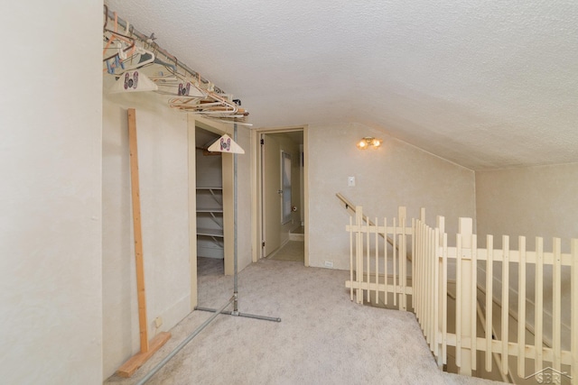 hallway with light colored carpet, a textured ceiling, and lofted ceiling