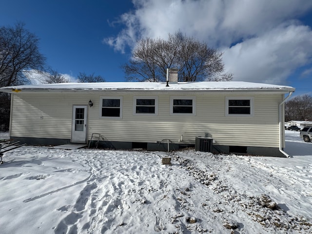 snow covered rear of property featuring central AC unit