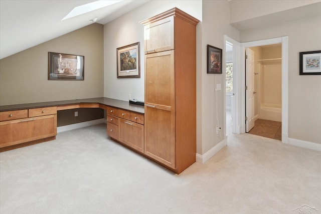 carpeted home office featuring built in desk and vaulted ceiling with skylight